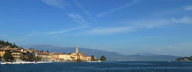 Wellnessurlaub beliebte Urlaubsziele am Gardasee -  Mit einer Fläche von 370 km² ist der Gardasee der größte See Italiens. Es liegt am Fuße der Alpen und erstreckt sich über drei Staaten: Lombardei, Venetien und Trentino. Die maximale Tiefe des Sees beträgt 346 m, er hat eine längliche Form und sein nördliches Ende ist sehr schmal. Dort ist der See von den Bergen der Gruppo di Baldo umgeben. Du trittst aus deinem gemütlichen Hotelzimmer und es begrüßt dich die warme italienische Sonne. Du blickst auf den atemberaubenden Gardasee, der in zahlreichen Blautönen schimmert - von tiefem Dunkelblau bis zu funkelndem Türkis. Majestätische Berge umgeben dich, während die Brise sanft deine Haut streichelt und der Duft von blühenden Zitronenbäumen deine Nase kitzelt. Du schlenderst die malerischen, engen Gassen entlang, vorbei an farbenfrohen, blumengeschmückten Häusern. Vereinzelt unterbricht das fröhliche Lachen der Einheimischen die friedvolle Stille. Du fühlst dich wie in einem Traum, der nicht enden will. Jeder Schritt führt dich zu neuen Entdeckungen und Abenteuern. Du probierst die köstliche italienische Küche mit ihren frischen Zutaten und verführerischen Aromen. Die Sonne geht langsam unter und taucht den Himmel in ein leuchtendes Orange-rot - ein spektakulärer Anblick.